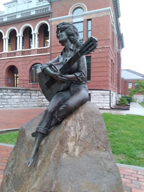 Dolly Parton statue with guitar and sitting on rock.