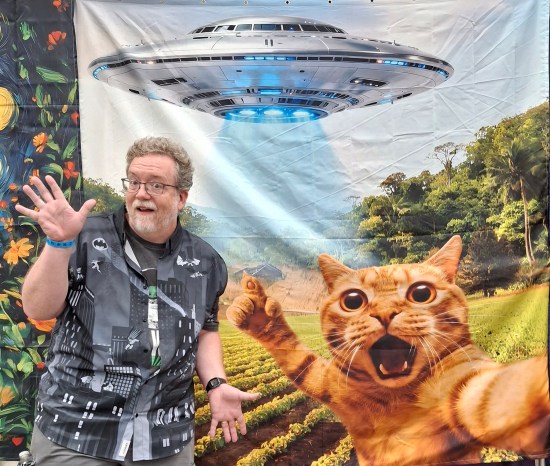 Me in front of a large picture of an orange tabby waving its paws frantically at a big UFO.
