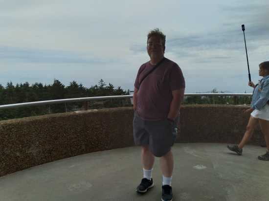 Me posing on aon observation deck. Behind me walks an Asian woman with a camera on a selfie stick.