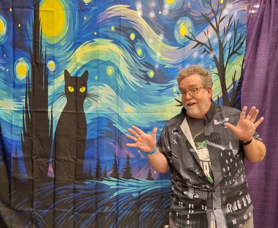 Me in black-and-white "Batman the Animated Series" shirt standing in front of a banner with a Starry Night homage that had a black cat added to it.