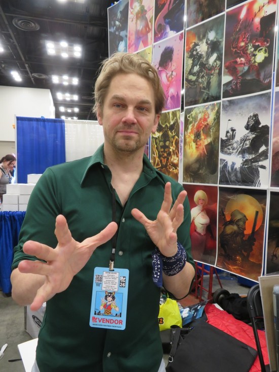 Stuart Sayger throwing hands, lots of paintings behind him.