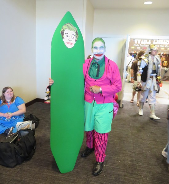 costume of Joker with green surfboard with pic of Joker's face on the end.