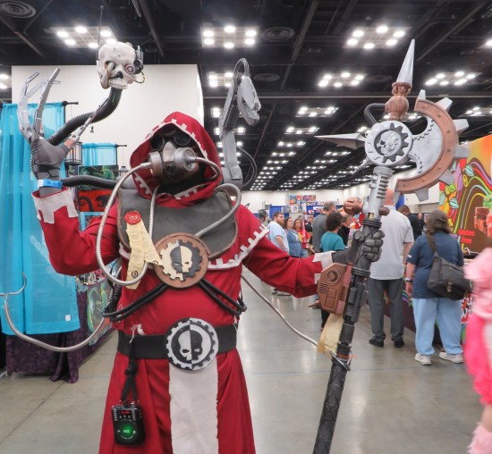 Tech Priest cosplay with red robe and multiple metal tentacles holding weaponry.