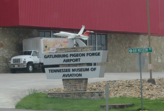 Sign for Tennessee Museum of Aviation with tiny plane on top, in front of a red furniture store.