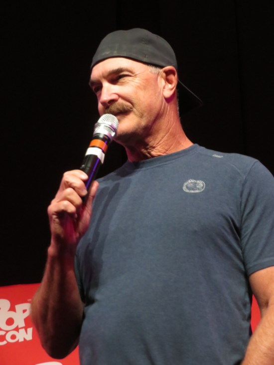 Warburton with mic and backwards hat, listening to a question.