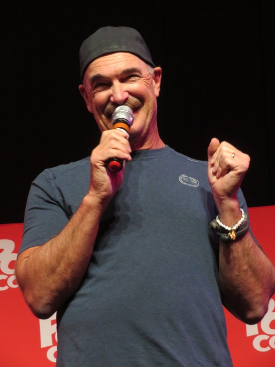 Patrick Warburton with mustache and mic, smiling.