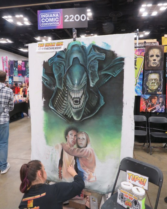 Artists sitting on floor, working on complicated chalk art of an Alien Queen, Ripley and Newt.