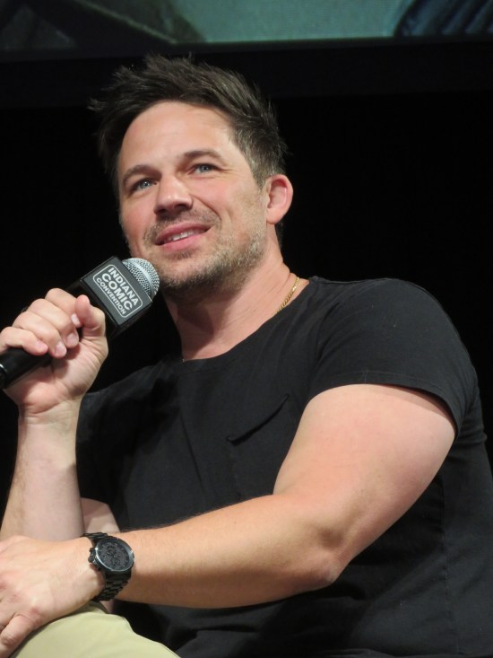 Matt Lanter leaning back in his chair, holding a mic and looking upward with his noticeably blue eyes.