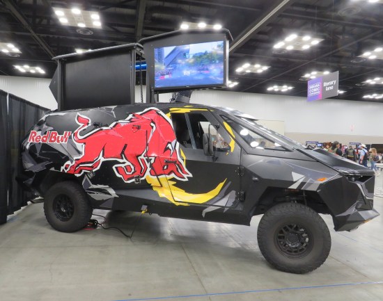 black Cybertruck with Red Bull logo painted on the side, parked inside a convention center.