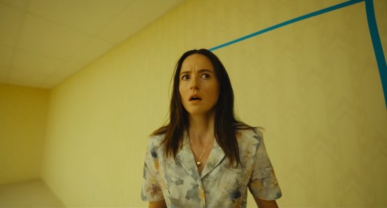 Therapist looks trepidatiously around an all-yellow room, seemingly empty except two blue strips of tape on the wall behind her.