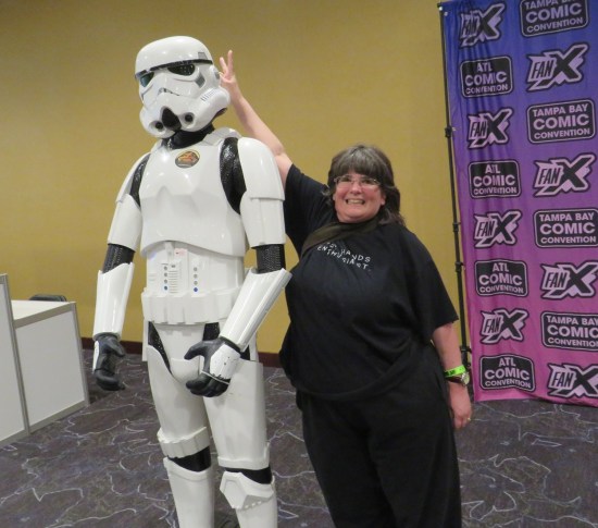 Anne standing behind a mannequin in Stormtrooper armor on a pedestal, reaching up to give it bunny ears.