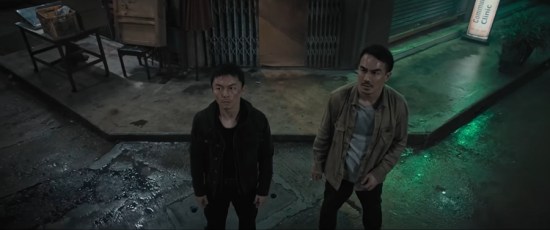 Two Asian men stand side-by-side on a grungy nighttime street, not happy.