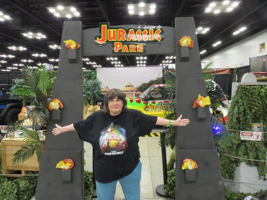 Anne standing, arms wide, in front of a Jurassic Park con booth.