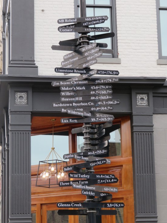 black post covered in arrow signs pointing to various locations with mileage counts.