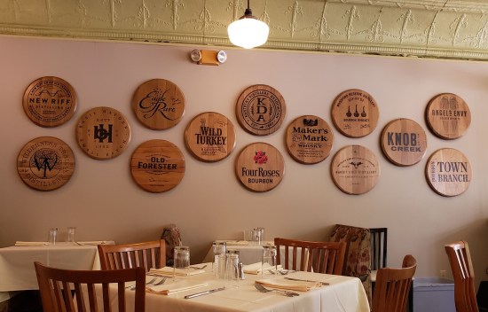 Restaurant wall decorated with 14 round wooden signs, each one with a different bourbon brand.