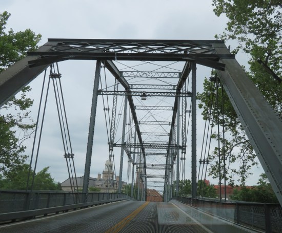 Two-lane bridge of black metal girders over river.