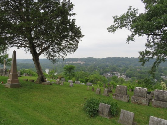 Hillside cemetery overlooking a city covered in leafy trees to the horizon.