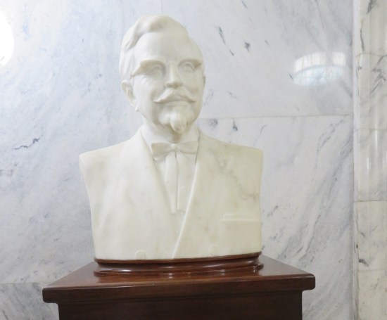 All white bust of Colonel Sanders in front of a white marble wall.