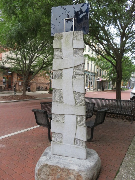Sculpture of tall white brick pillar wrapped in large bandages and a black box on top.