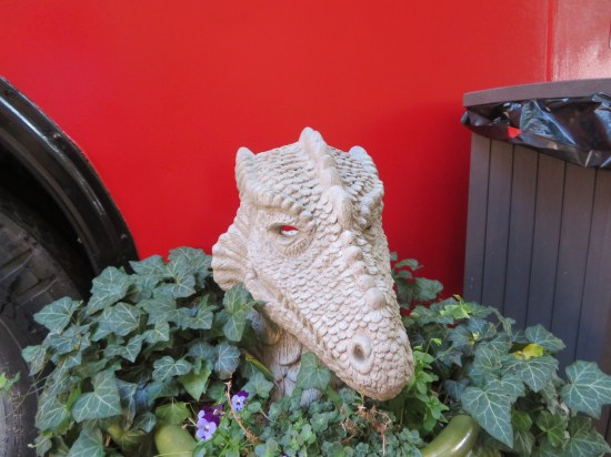 White stone dragon head atop a large outdoor planter next to a red bus.