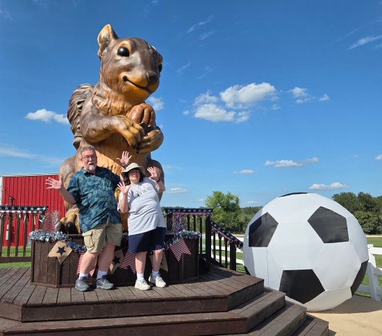 Us doing jazz hands in front of a giant squirrel statue. Next to the platform is a giant inflatable soccer ball.