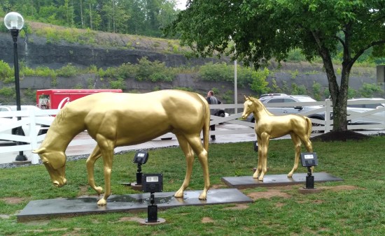 Two golden horse statues, posed as if they're chewing grass, in the middle of a rest stop lawn.
