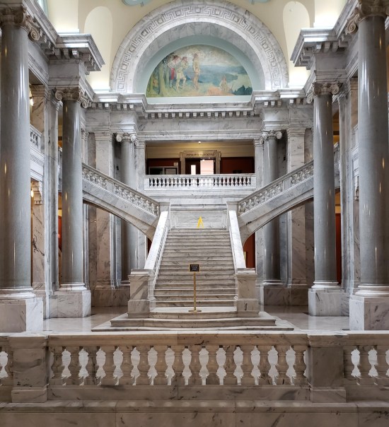 marble staircase that splits into a T and continues up each way. Columns and Greco-Roman architecture abounds.