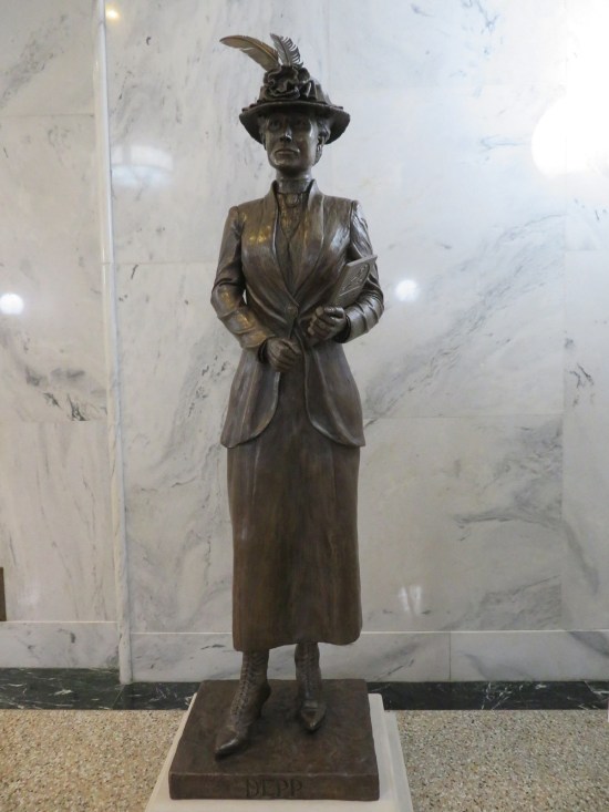 Nettie Depp statue, holding a textbook and wearing a fancy hat with two feathers and a big flower.