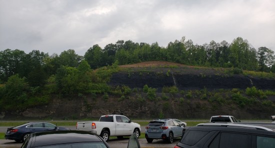 sizable cliff along an interstate. Cars are parked on our near side.