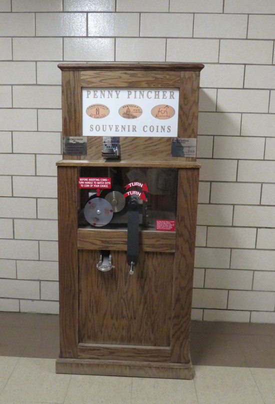 smashed penny machine against white brick wall