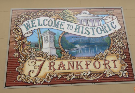 mural with flowery title Welcome to Historic Frankfort with images of Old State Capitol, Kentucky River, and a stone pedestal.
