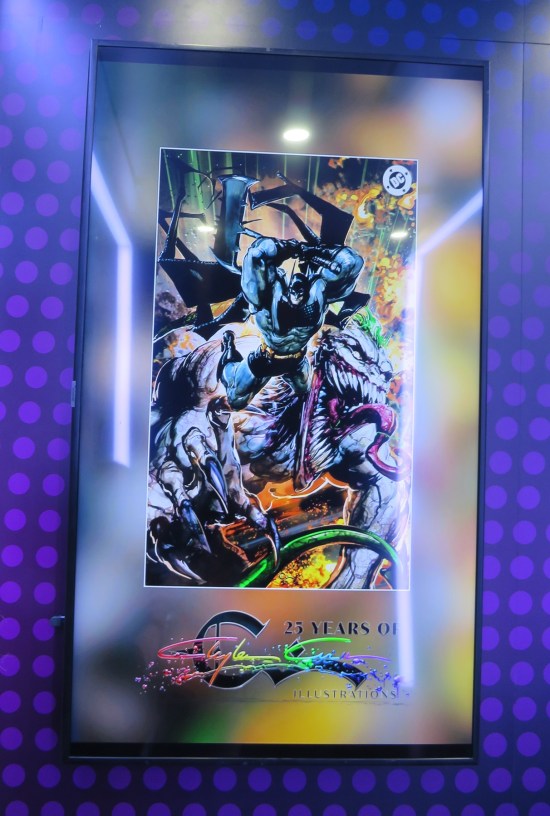 Tall wall-mounted monitor showing art with Absolute Batman clobbering Absolute Joker.
