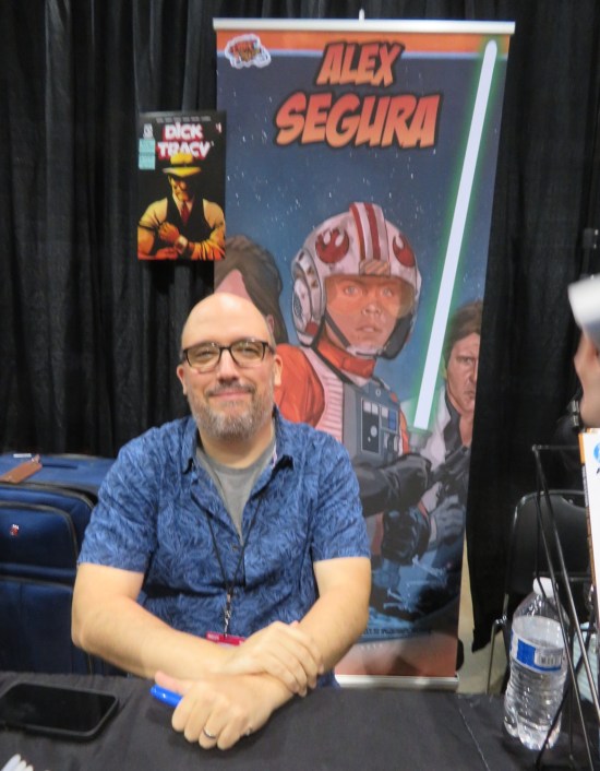 Alex Segura at his booth, decorated with images of Dick Tracy and Luke Skywalker in X-Wing Pilot uniform.