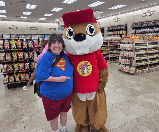 Anne smiling and pointing next to an employee in a furry Buc-eee suit. Behind them are gas station snack displays.
