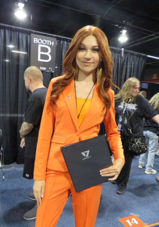Ashley Barrett cosplayer in orange business suit, carrying a planner.