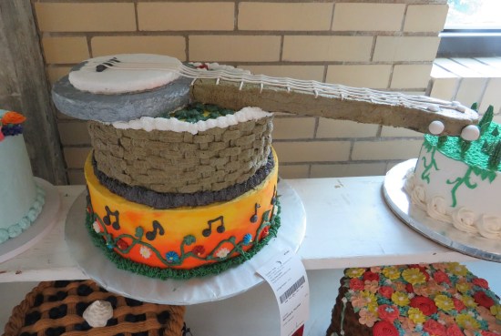 two-layer music themed cake with a third banjo-shaped layer jutting way out on top.