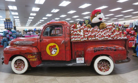 Red truck with Buc-ee branding on the door. Back is filled with stuffed Buc-ees. It's parked in the department store section.