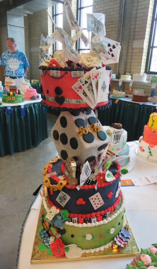 Tall 4-layer cake with playing cards sticking out. The second level is shaped like a six-sided die standing on its corner.