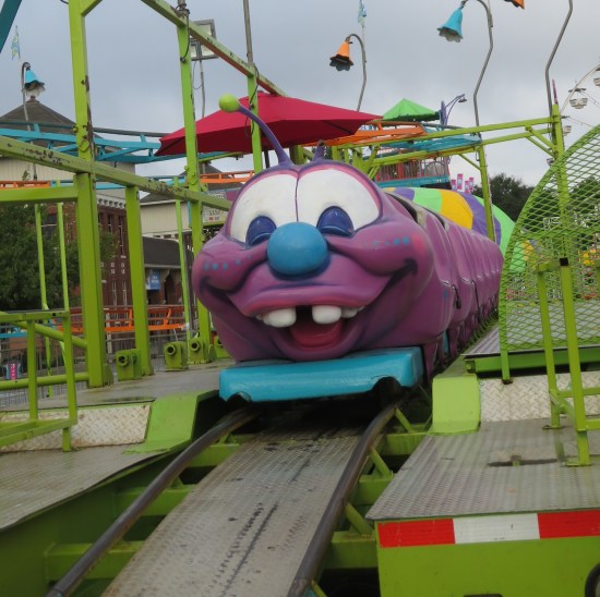 Purple caterpillar roller coaster for kids on green track, no people around.
