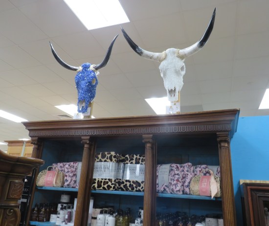 two cattle skulls, one blue and one white, atop a cabinet filled with bedding.