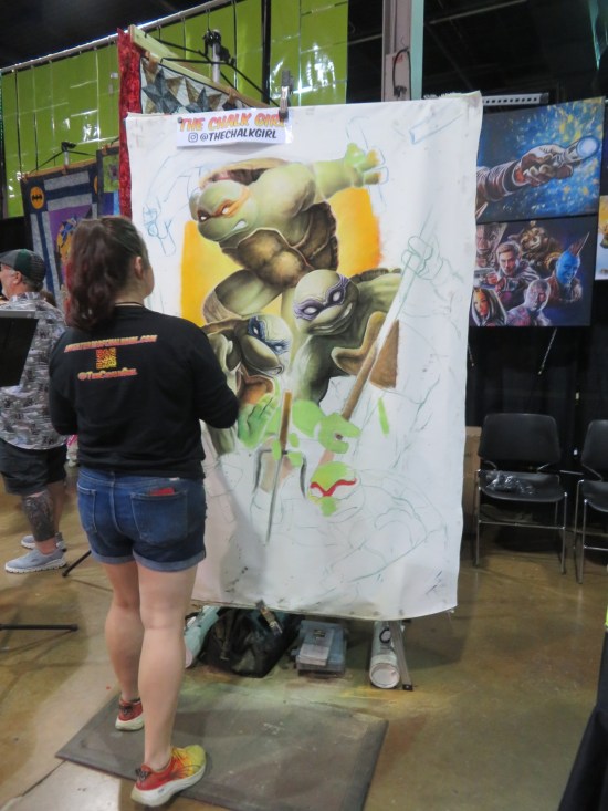 Young lady painting the TMNT, three of whom are mostly done.