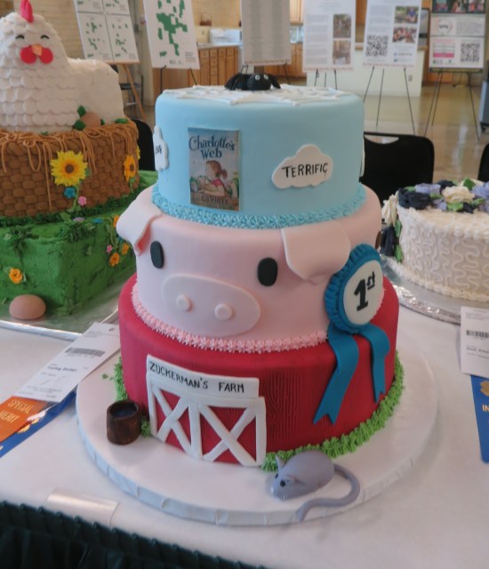 Three-layer cake with a barn bottom, pig head middle, and a spider topper.