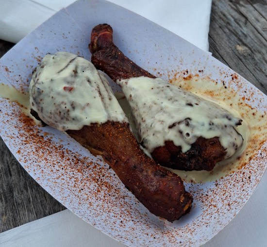 Two small drumsticks in a paper dish covered in red spices and a white sauce with green flecks.