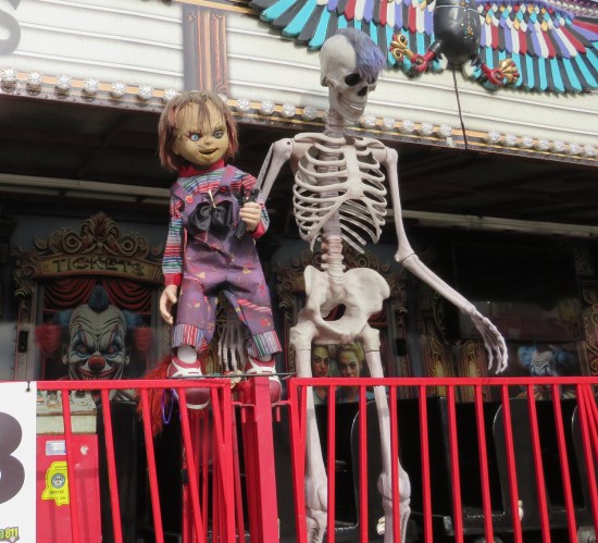 Chucky doll and a skeleton with a purple mohawk glued to its skull are fastened to the front of a spooky fun house.