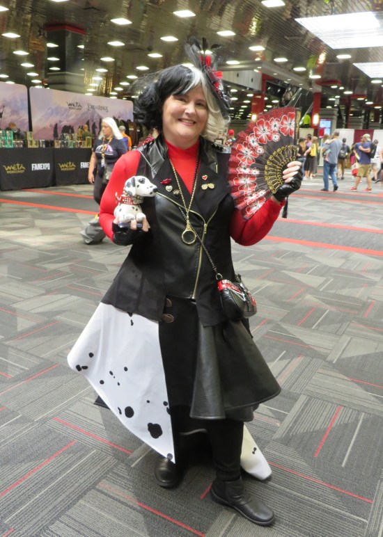 stylized Cruella De Vil costume with stuffed Dalmatian puppy, red and black fan, and long-tailed overcoat.