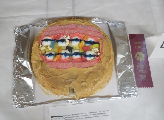 Brown cake topped with icing drawing of crooked teeth with braces.