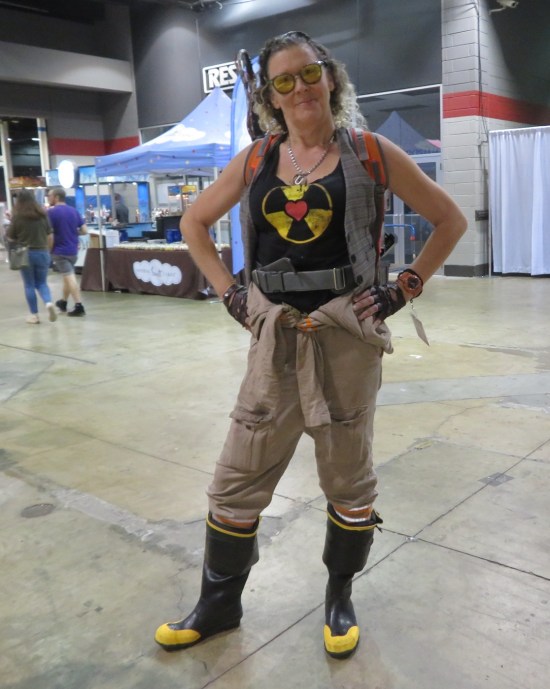 Blond female Ghostbuster with black T-shirt sporting radioactive symbol with a heart in the middle.