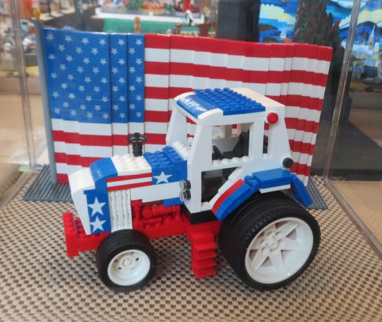 Lego tractor entirely red, white and blue with Lego flag standing behind it.