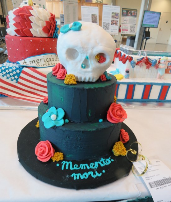 Cake shaped like top hat with cartoon skull on top.