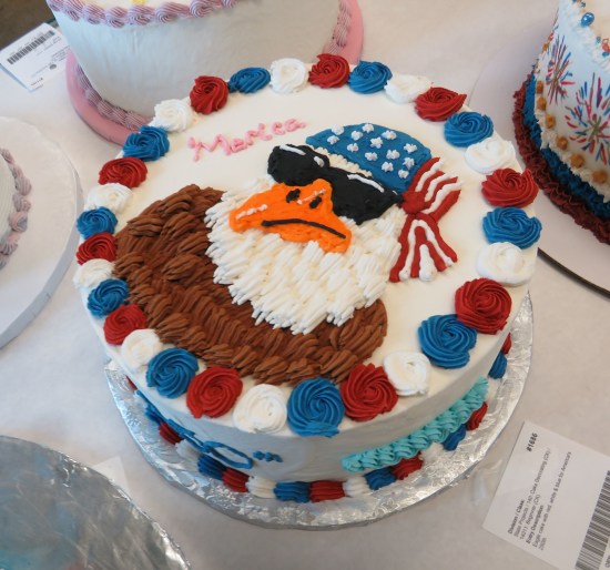 White cake with icing picture of bald eagle wearing sunglasses and a US flag bandanna on its head. Next to it is written "'Merica" in red icing.